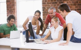 Five businesspeople in office space looking at computer and smil