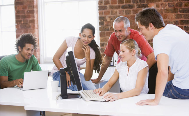 Five businesspeople in office space looking at computer and smil